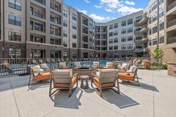 An outdoor lounge area with a fire pit and lounge chairs in front of an apartment building